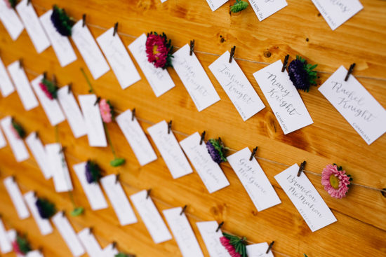 wildflower escort card display on a wooden board - grey calligraphy on white paper with colorful florals